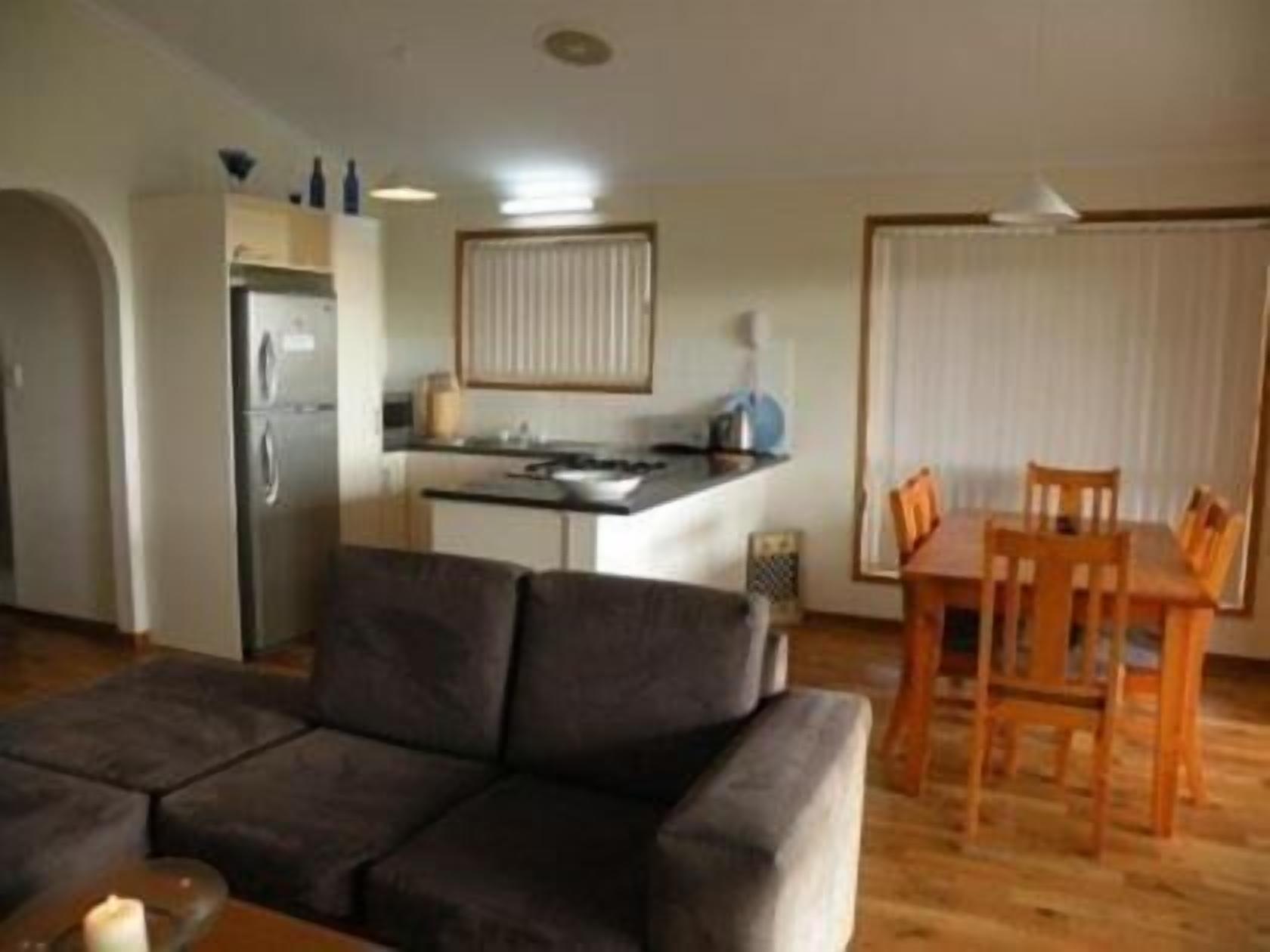 A compact living space with a kitchenette, a dining area with wooden chairs, and a sofa.
