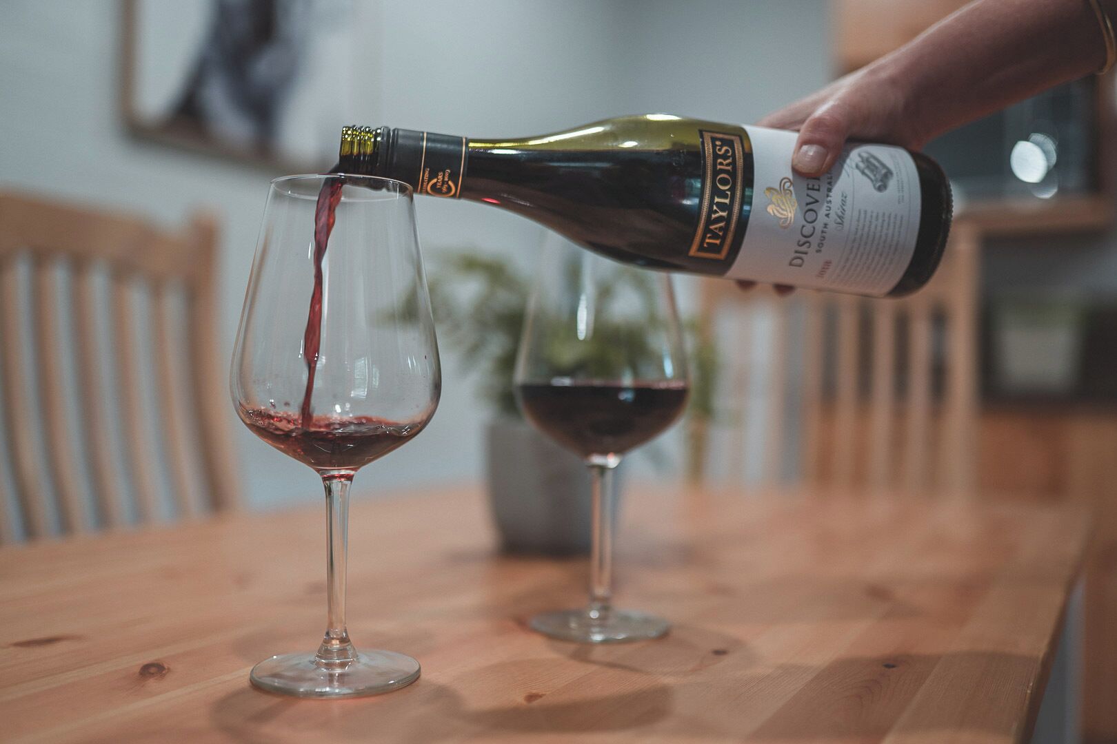 A hand pouring wine from a bottle into a glass on a wooden table.