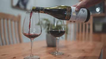 A hand pouring wine from a bottle into a glass on a wooden table.