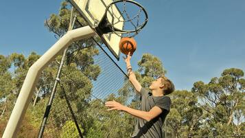A person playing basketball on an outdoor court with trees in the background.