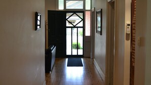 A hallway with wooden flooring, a black door at the end, and a light switch on the wall. - Tin House at Tanunda (Tanunda)
