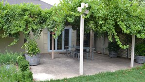 A covered patio area with a table and chairs, surrounded by potted plants and a grassy area. - Tin House at Tanunda (Tanunda)
