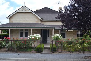 A two-story house with a porch, a front door, and a small front yard with flowers. - Tin House at Tanunda (Tanunda)