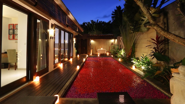 Un sendero de guijarros rojos que lleva a un área de comedor con una mesa y sillas, rodeada de plantas y velas.