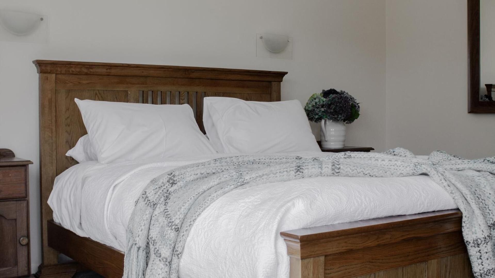 A neatly made bed with a wooden headboard, white pillows, and a white throw blanket.
