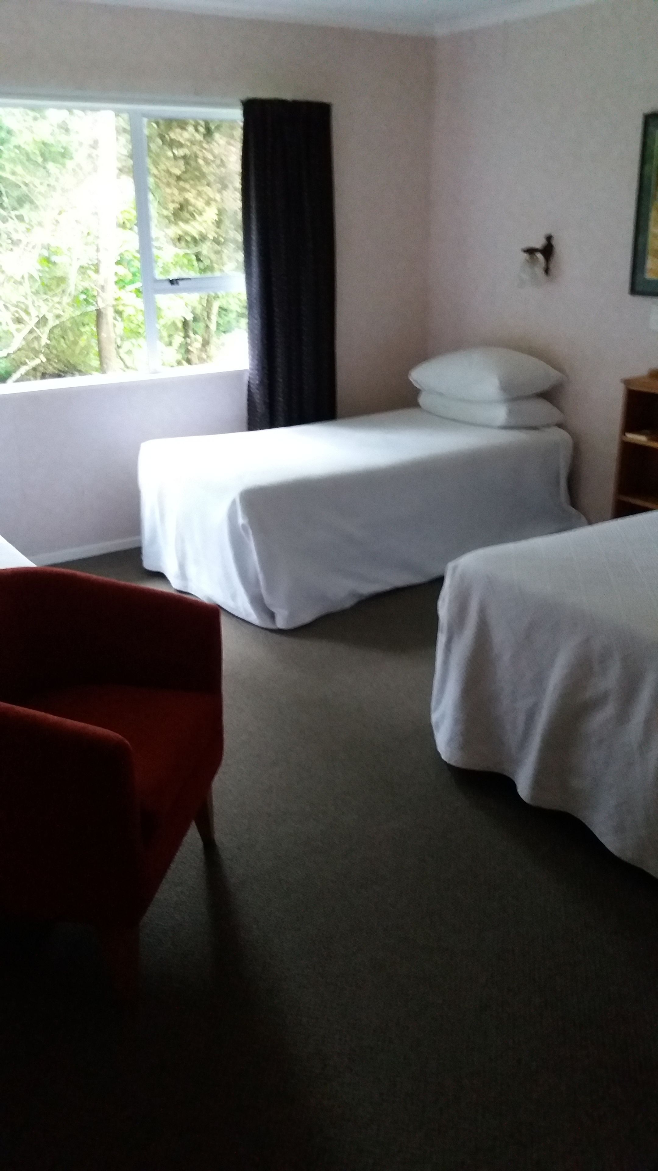 Habitación de hotel con dos camas individuales, una silla roja, una mesita de noche y una ventana con cortinas.