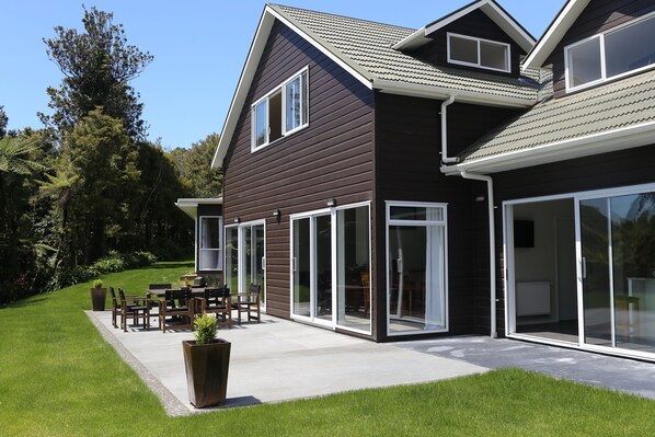Une maison moderne dotée d’un patio, de grandes portes-fenêtres coulissantes et d’une pelouse bien entretenue.