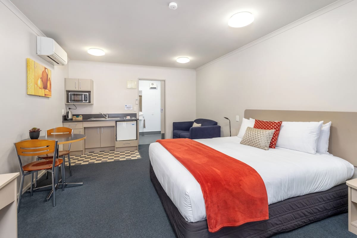 A hotel room with a bed, a desk, a chair, a microwave, and a kitchenette.
