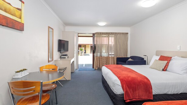 Habitación de hotel con cama, escritorio, silla, televisión y vistas al exterior.