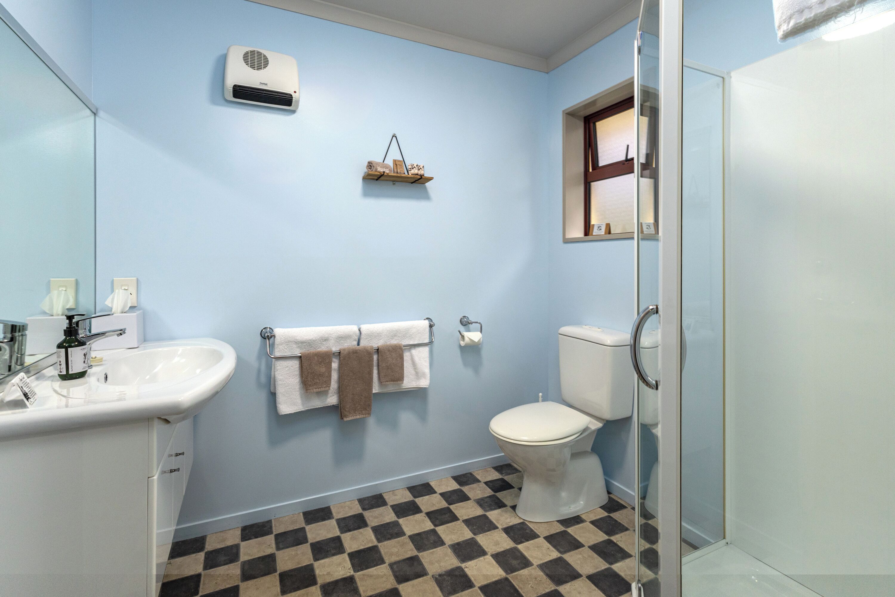 Een badkamer met een witte wastafel, een toilet, een douchecabine van glas en een zwart-wit betegelde vloer.