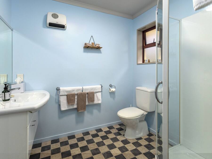 Un baño con un lavamanos blanco, inodoro, cabina de ducha de vidrio y suelo a cuadros.