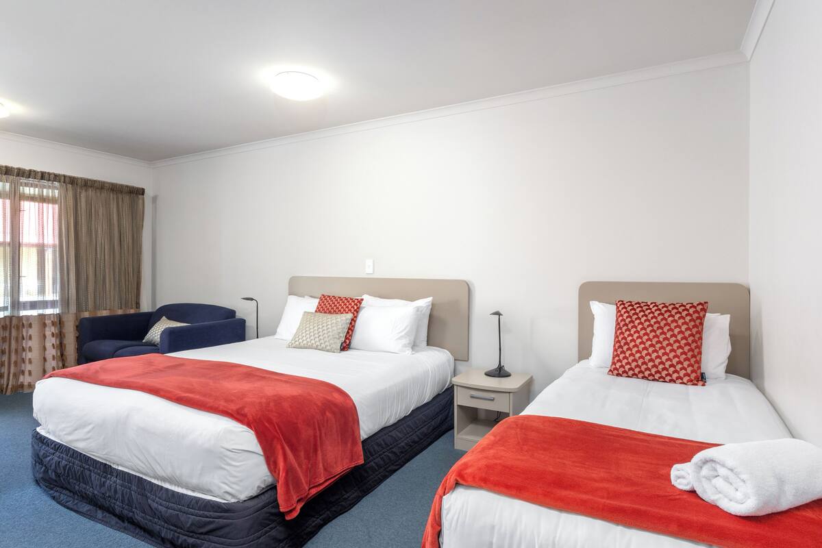 A hotel room with two beds, a desk, a chair, and a window with curtains.