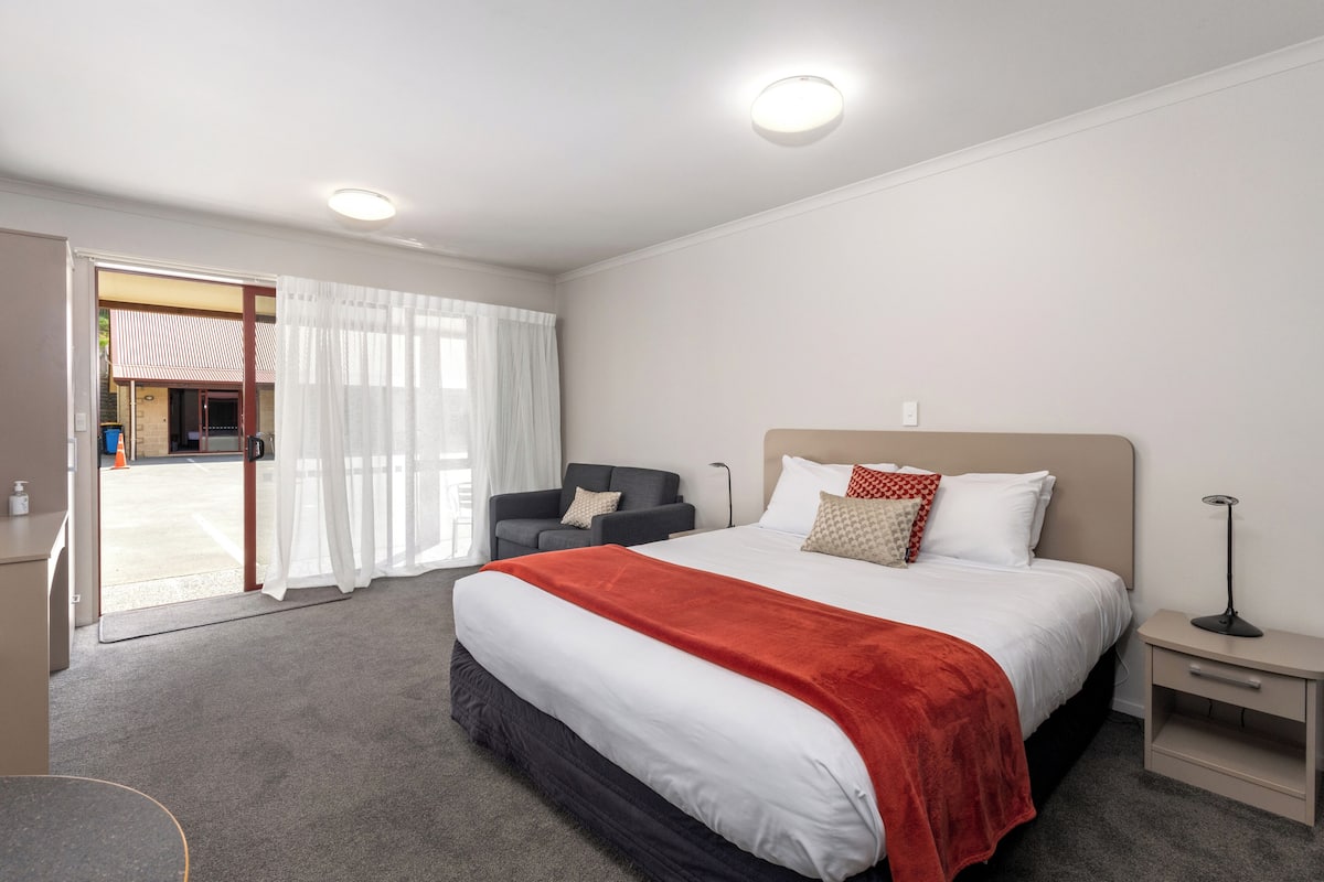 A hotel room with a large bed, a desk, a chair, and a nightstand.