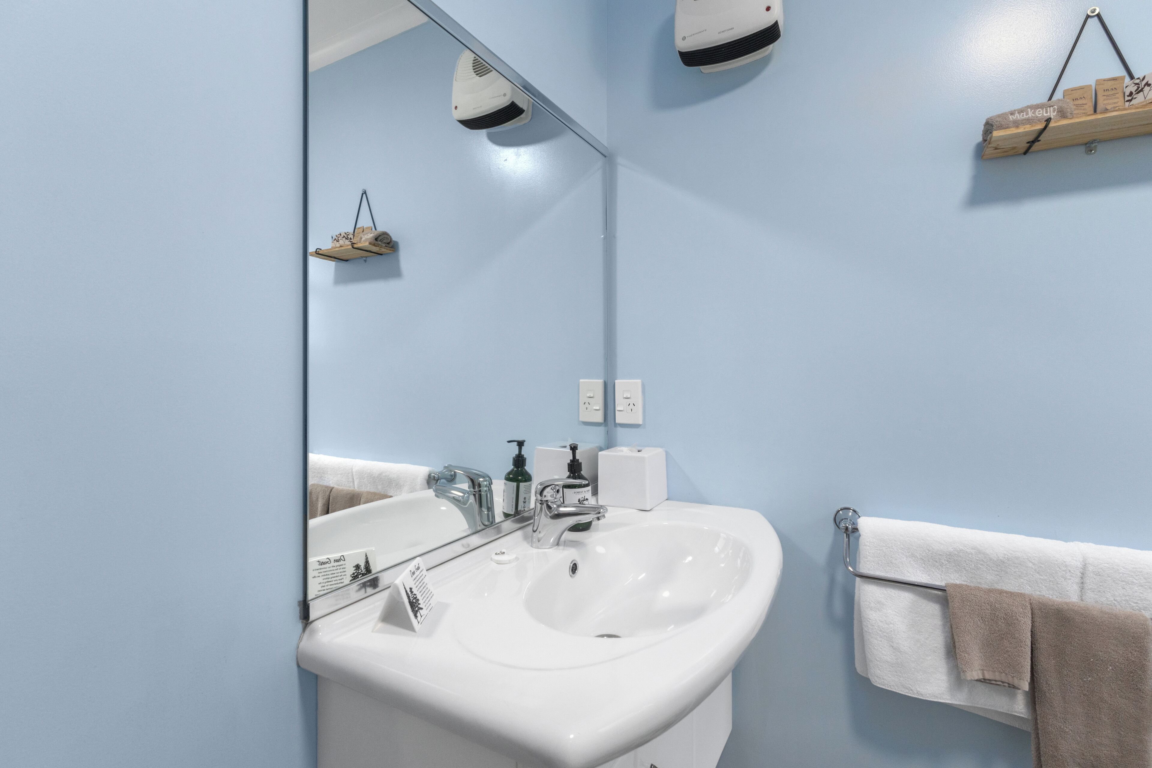 Un baño con lavamanos blanco, espejo y toallero.