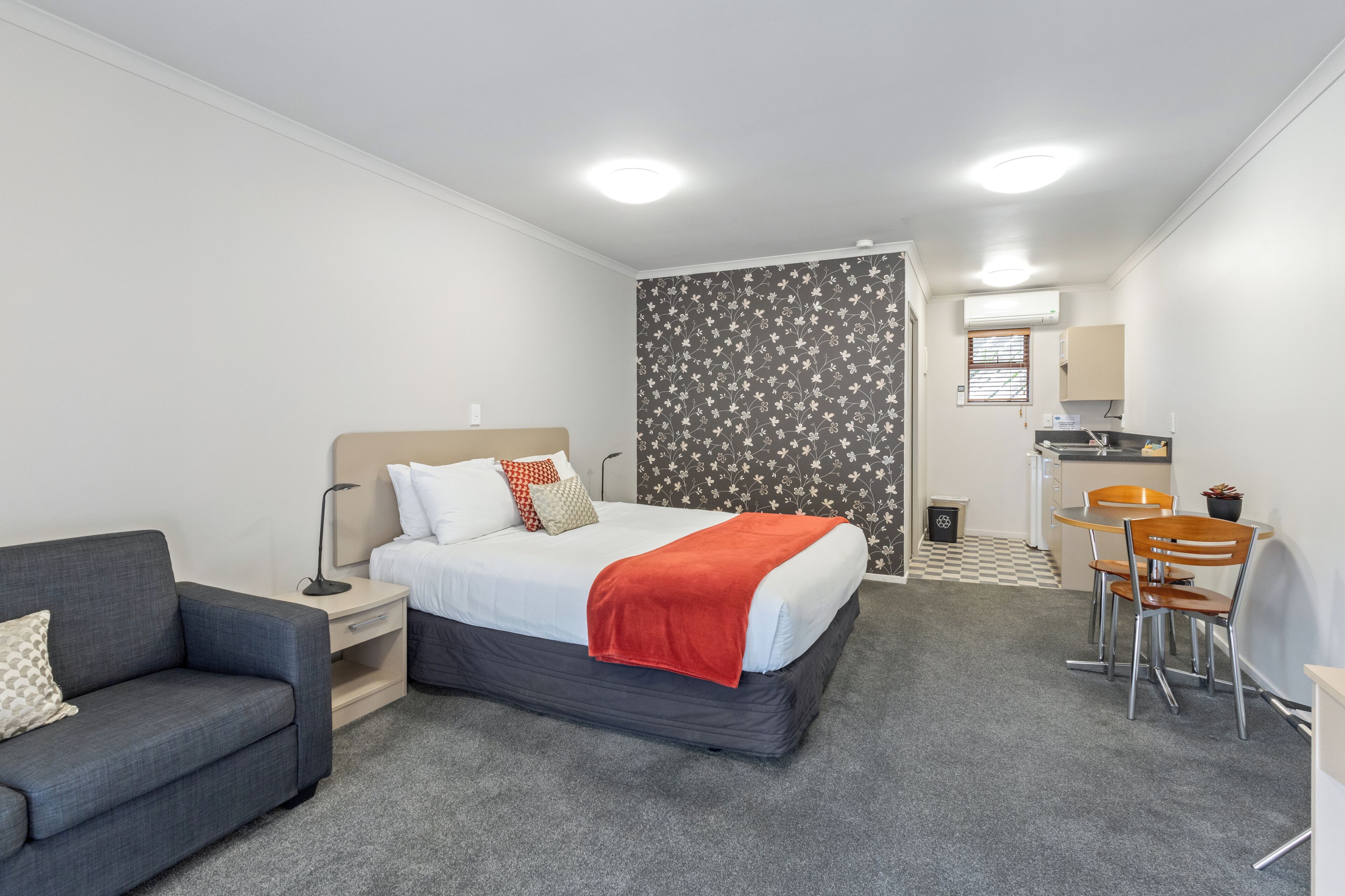 A hotel room with a bed, a desk, a chair, and a small kitchenette.