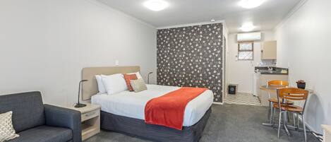 Una habitación de hotel con cama, escritorio, silla y una pequeña cocina.