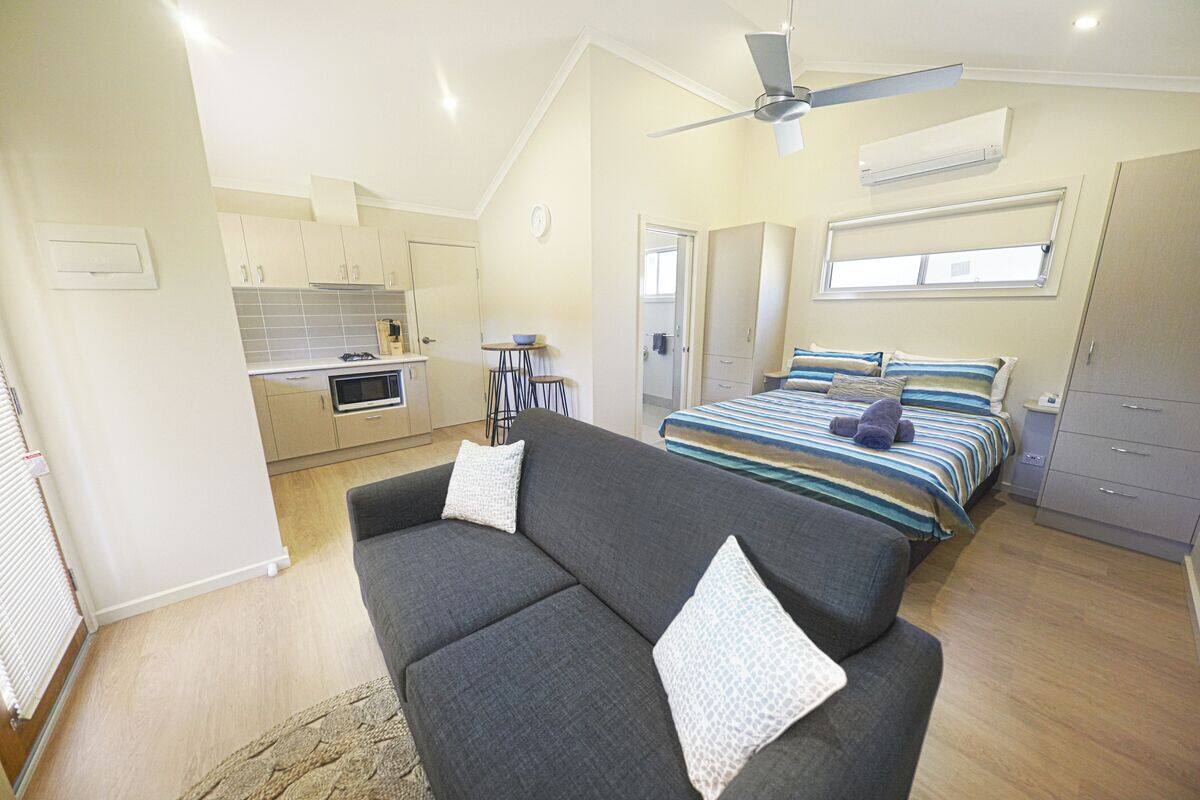 A compact bedroom with a bed, a sofa, a small kitchenette, and a ceiling fan.