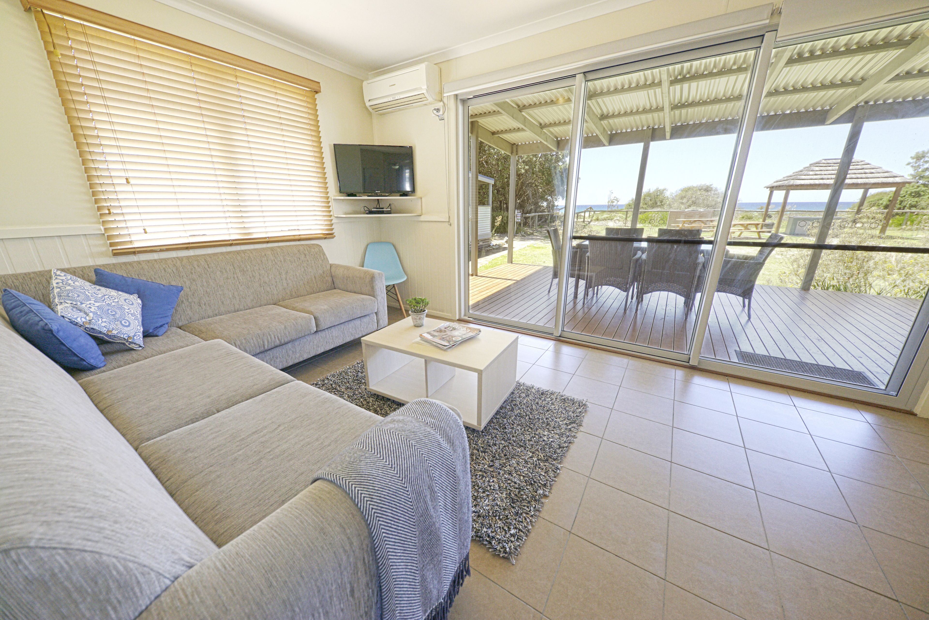 A living room with a sofa, a coffee table, and a TV. There is a sliding glass door leading to an outdoor deck.