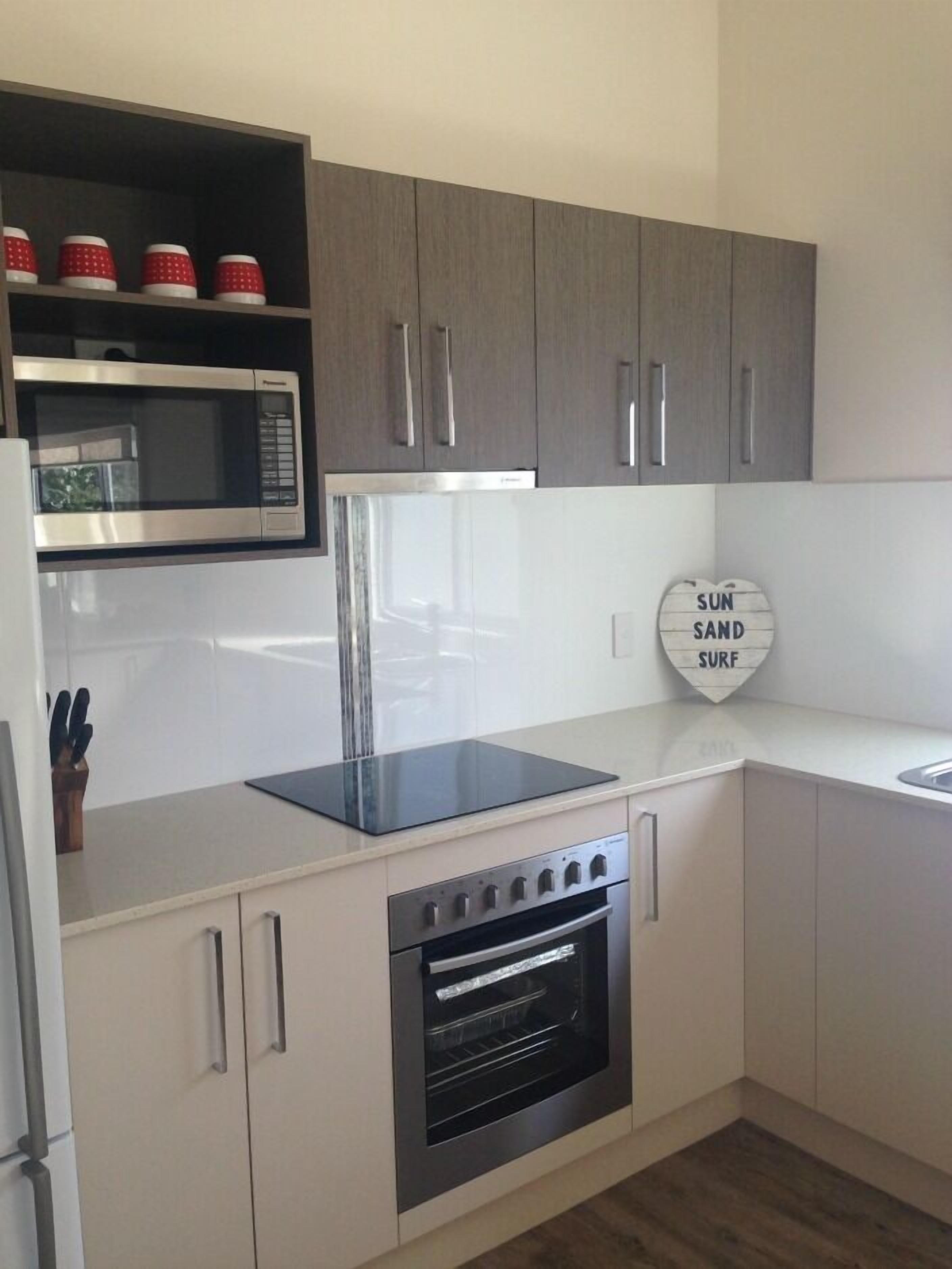 A modern kitchen with grey cabinets, a built-in microwave, a black induction cooktop, and an oven.