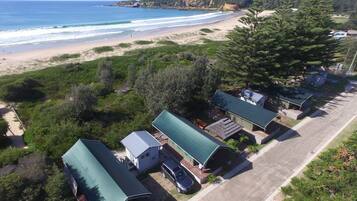 A coastal property with multiple green-roofed cabins, a beach, and a forested area.