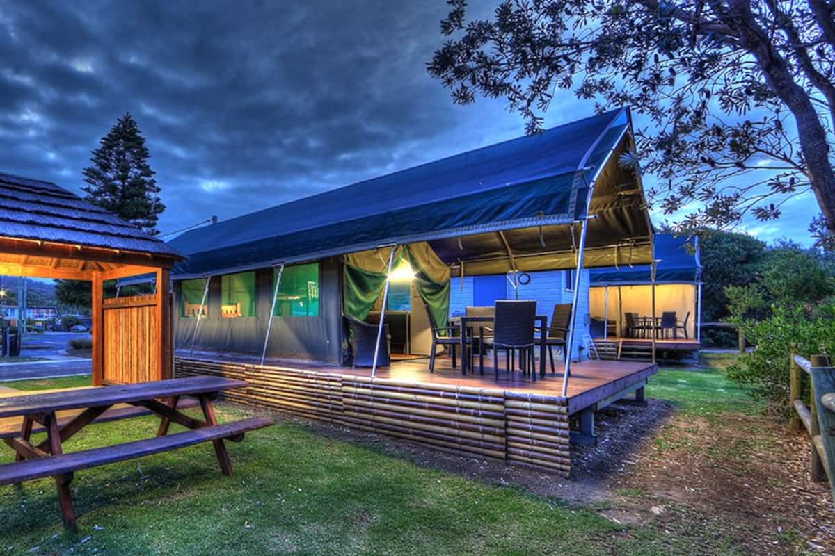 A rustic outdoor dining area with a wooden pavilion and picnic table, adjacent to a covered seating area with a view of the surrounding landscape.