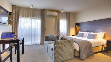 Una habitación de hotel con cama, escritorio con computadora portátil, sofá y televisor.