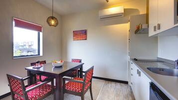 A compact kitchen with a dining area, featuring a modern design with white cabinets, a built-in dishwasher, and a dining table with red patterned chairs.