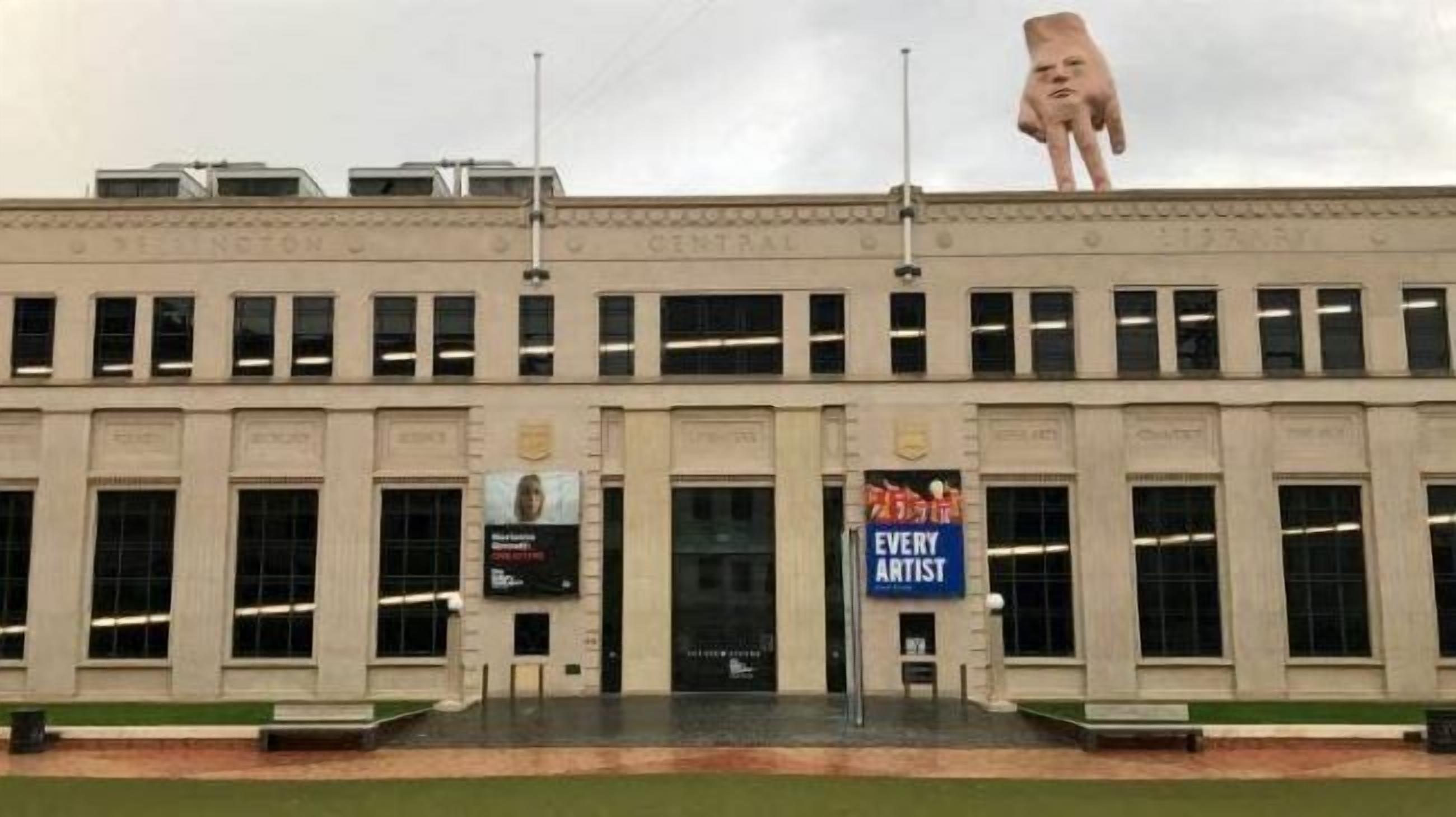 Un edificio con una gran escultura de una mano en la parte superior.