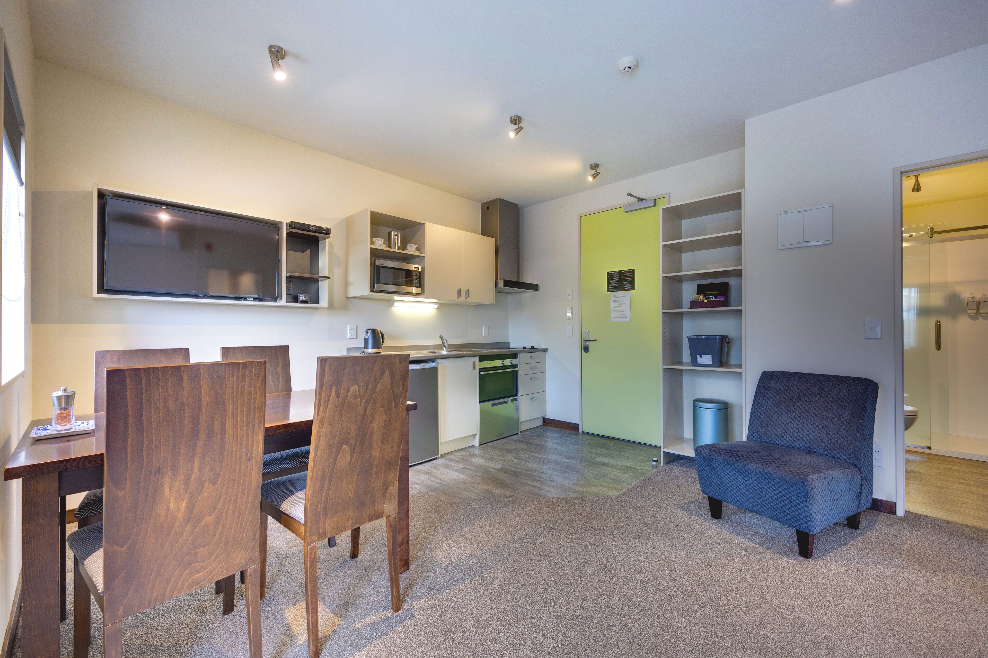 Une cuisine moderne dotée d’appareils électroménagers intégrés, un coin repas avec des chaises en bois et un petit espace salon avec un fauteuil bleu.