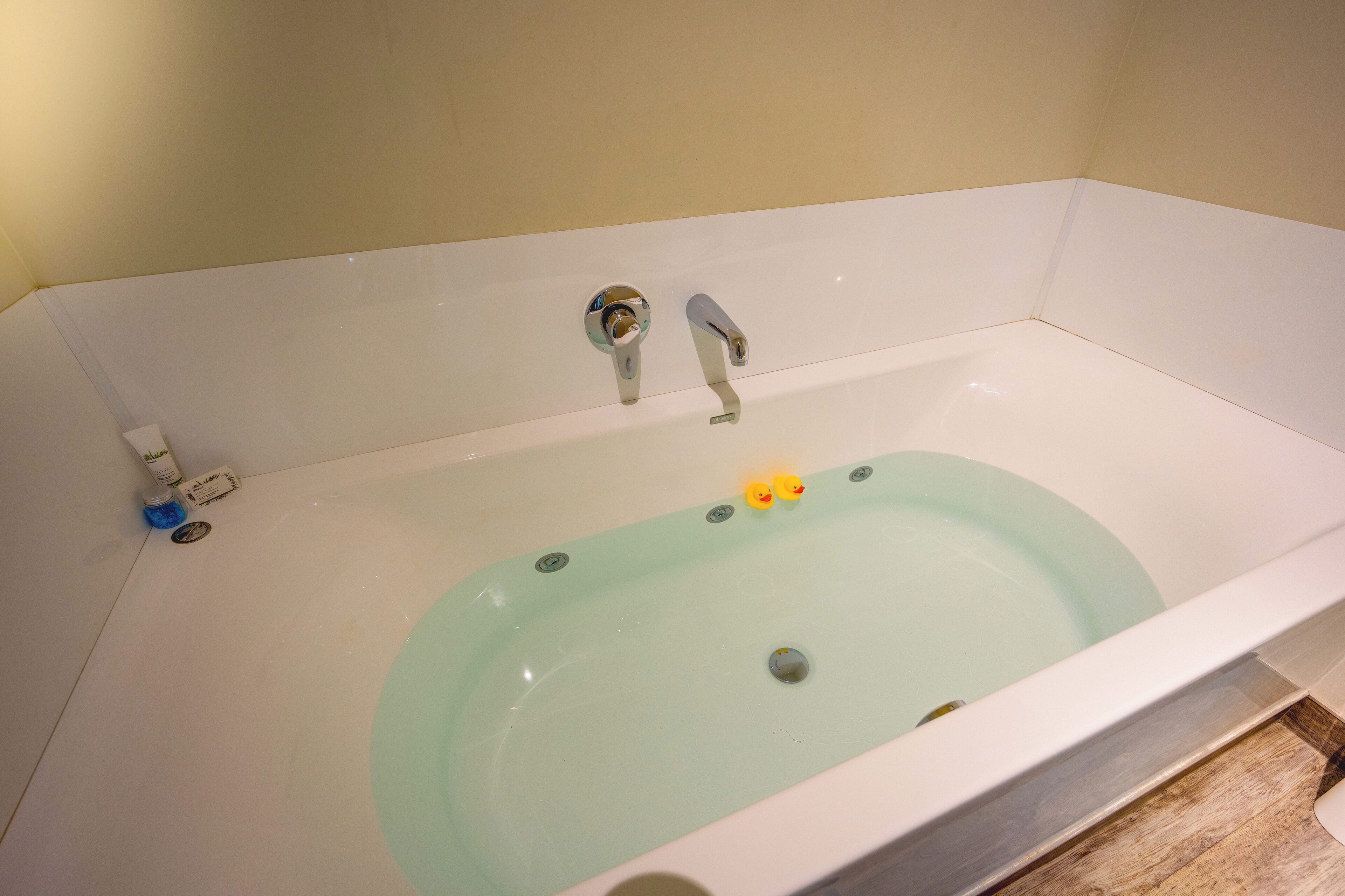 A bathtub with a greenish tint, two faucets, and a drain.