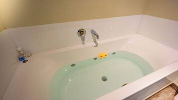 A bathtub with a greenish tint, two faucets, and a drain.