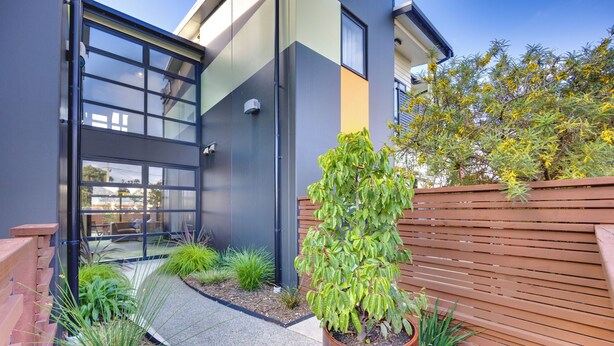 A modern building with large windows, a wooden fence, and a variety of plants. - Ava Lodge (Lower Hutt)