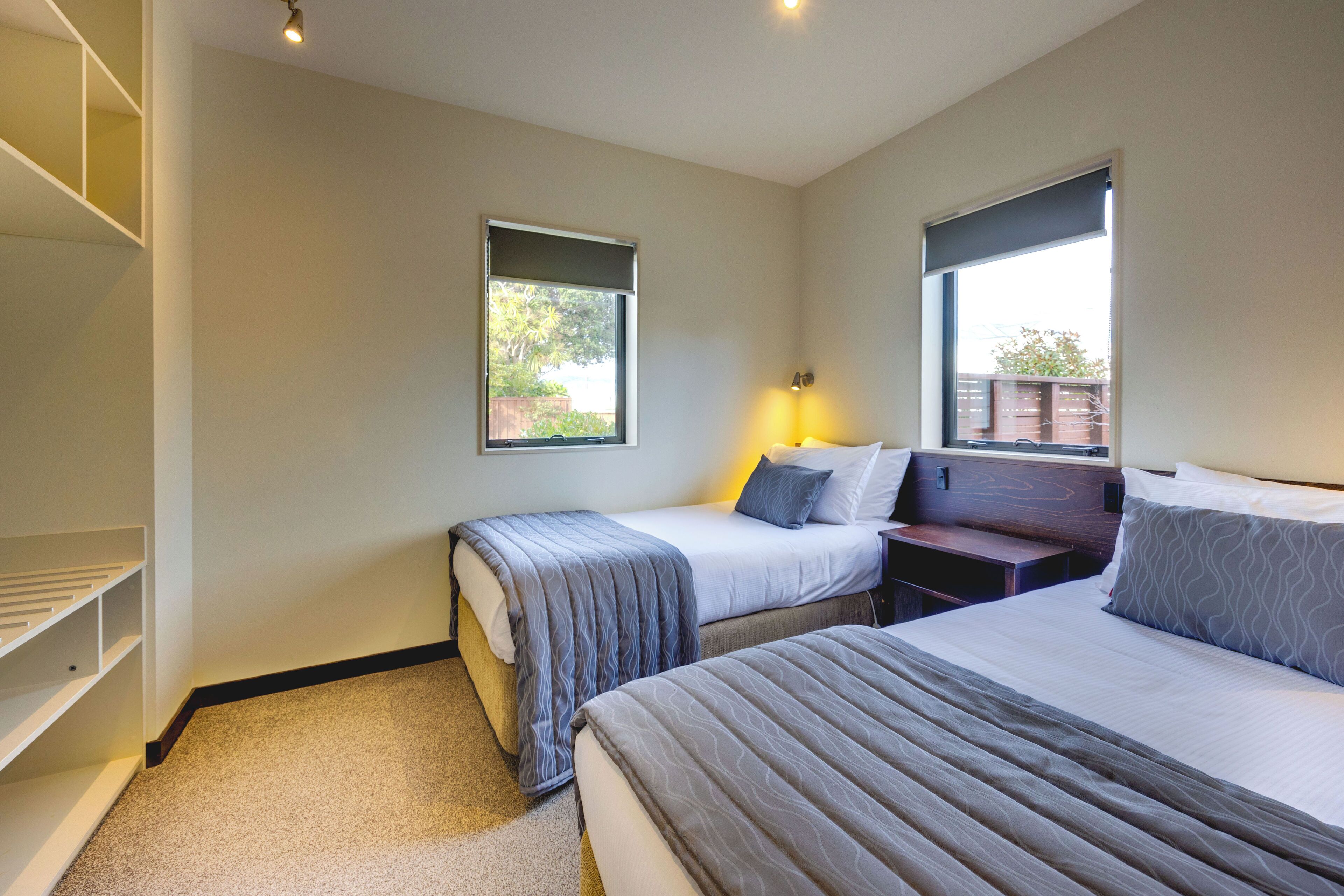 A bedroom with two beds, a bedside table, a lamp, and a window.