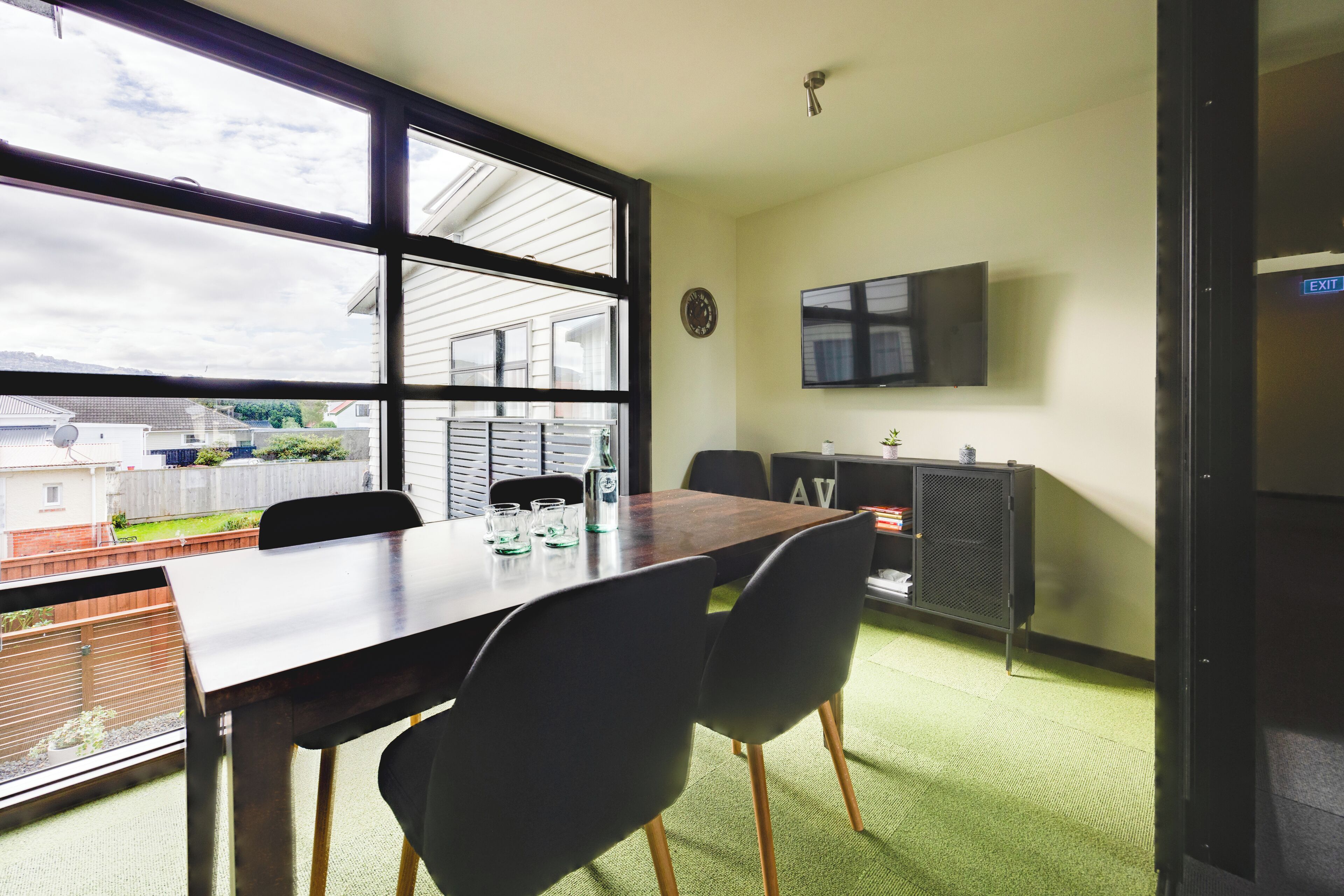 A conference room with a large table, four chairs, a clock, and a TV mounted on the wall.