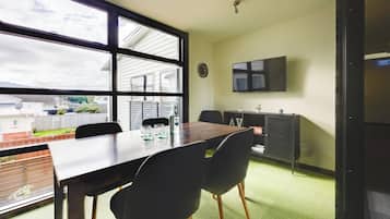 A conference room with a large table, four chairs, a clock, and a TV mounted on the wall.