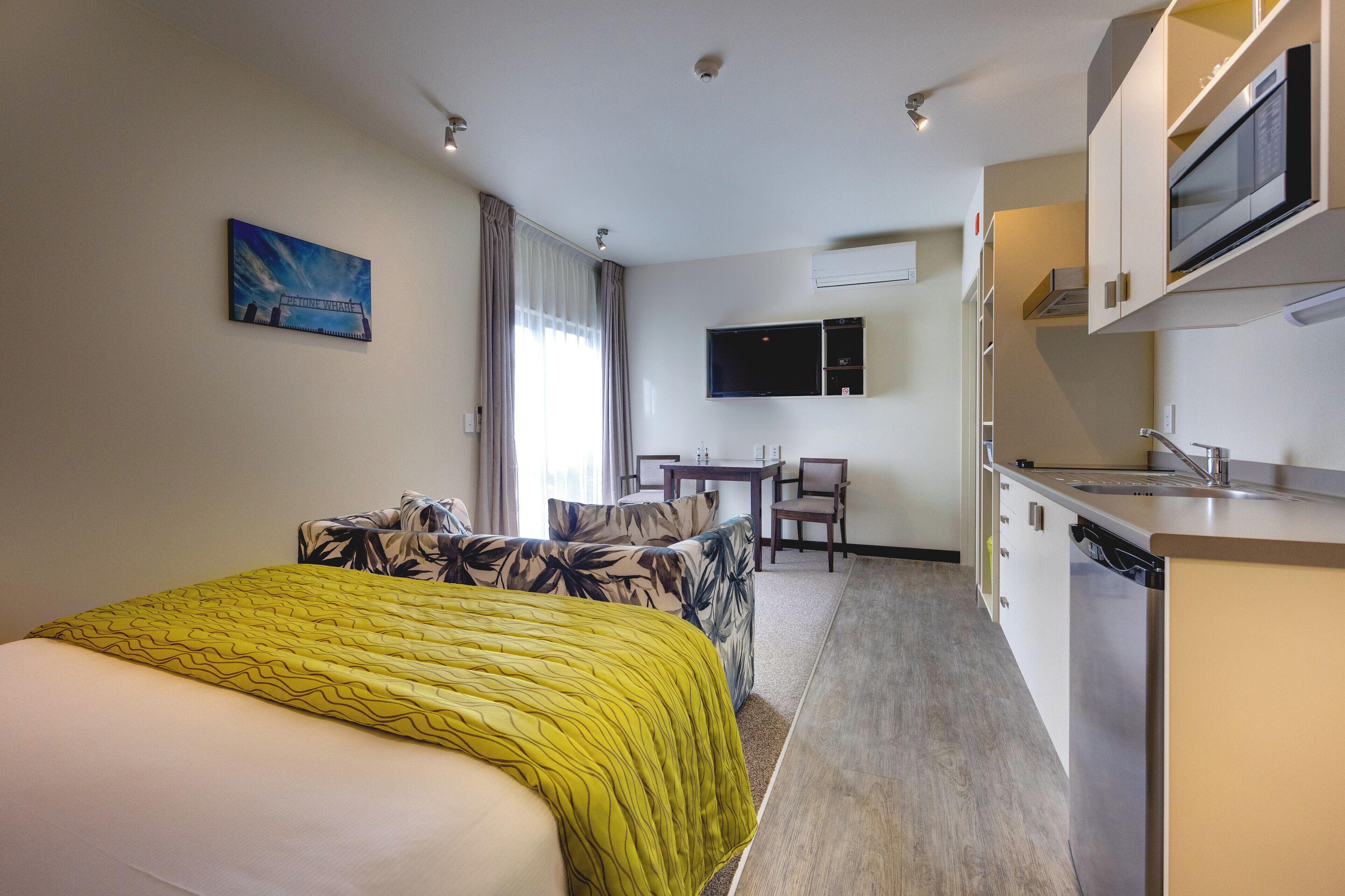 Hotelkamer met een bed, een sofa, een kitchenette en een aan de muur bevestigde televisie.
