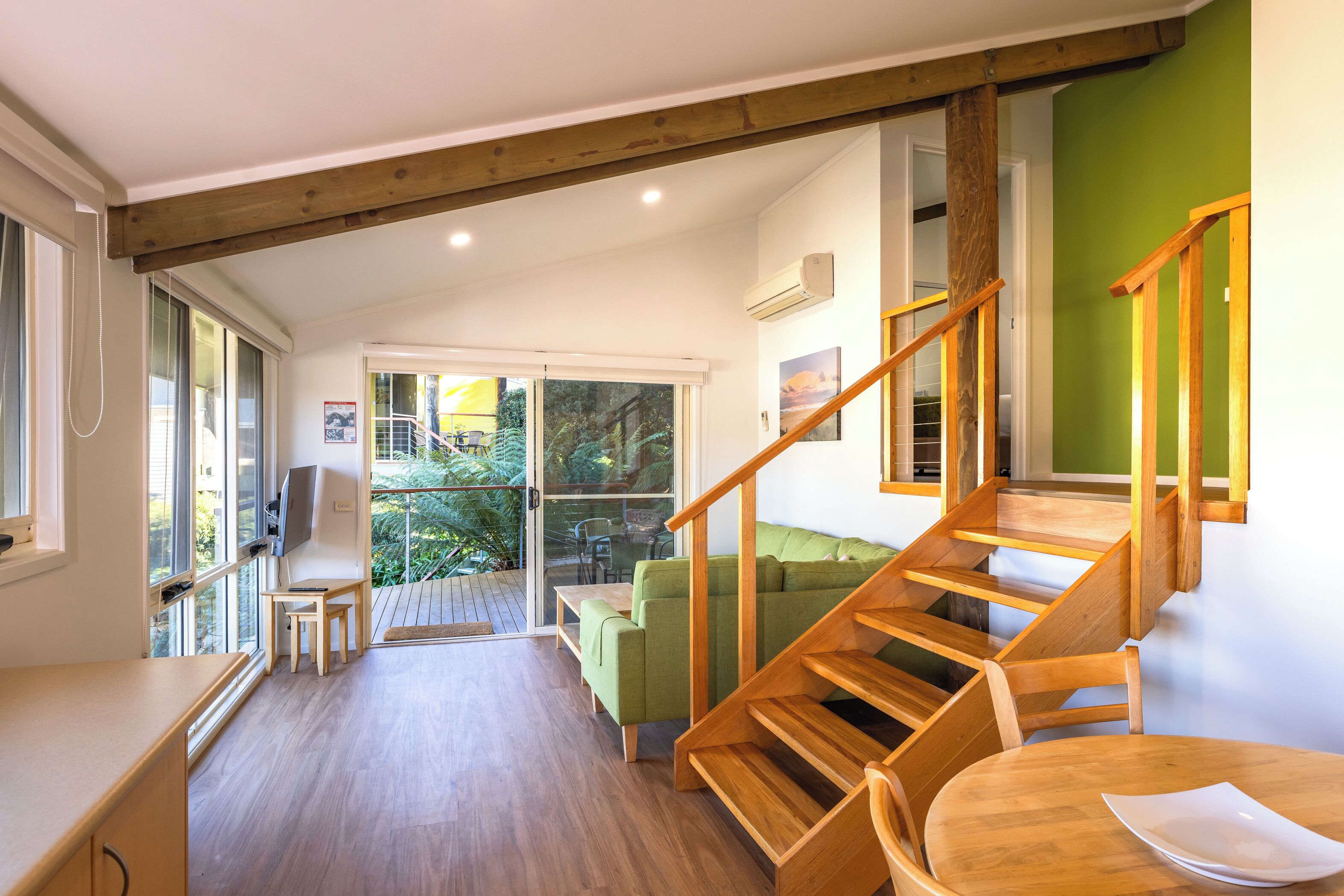 A modern interior with a wooden staircase, a green sofa, and a dining area.