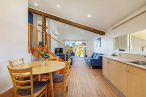 Una cocina moderna con armarios de madera, un comedor con una mesa redonda y sillas, y una escalera que lleva a un balcón.