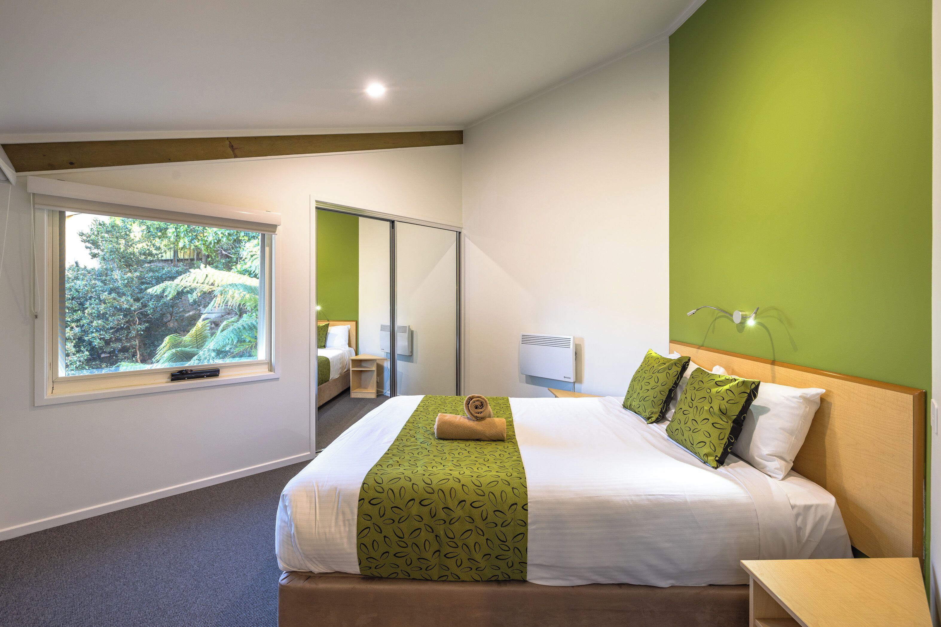Habitación de hotel con cama, ventana con vistas a la vegetación, mesita de noche y aire acondicionado de pared.