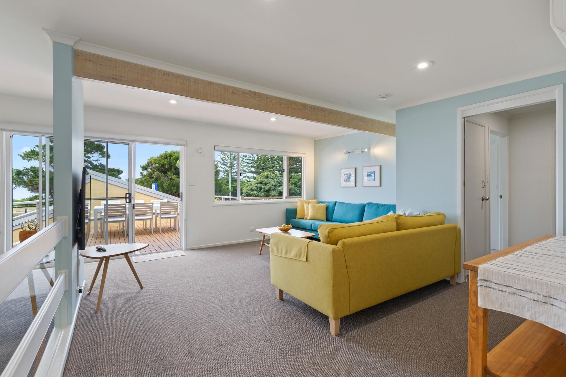 A spacious living area with a yellow sofa, a small table, and a balcony with outdoor furniture.