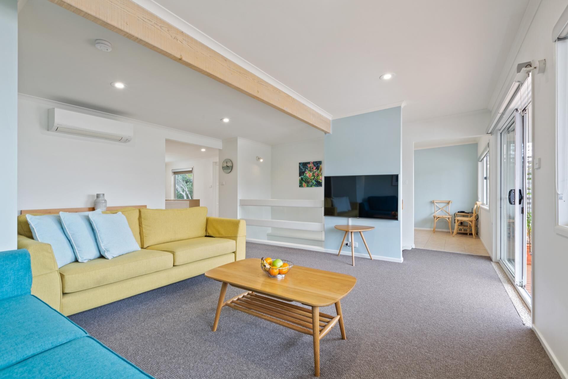 Ein modernes Wohnzimmer mit einem gelben Sofa, einem Holztisch und einem Fernseher.