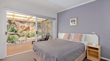 A bedroom with a large bed, a nightstand, a window with a view of a garden, and a ceiling fan.