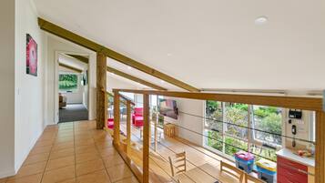 Una habitación amplia con techo alto, una escalera de madera, un área de comedor con sillas y vistas al exterior.