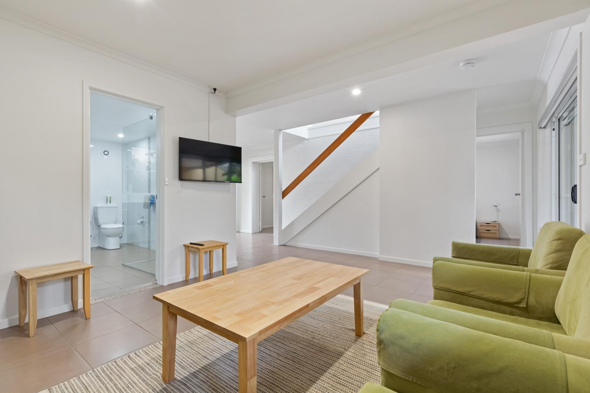 A modern living room with a wooden coffee table, green sofa, and a TV mounted on the wall.
