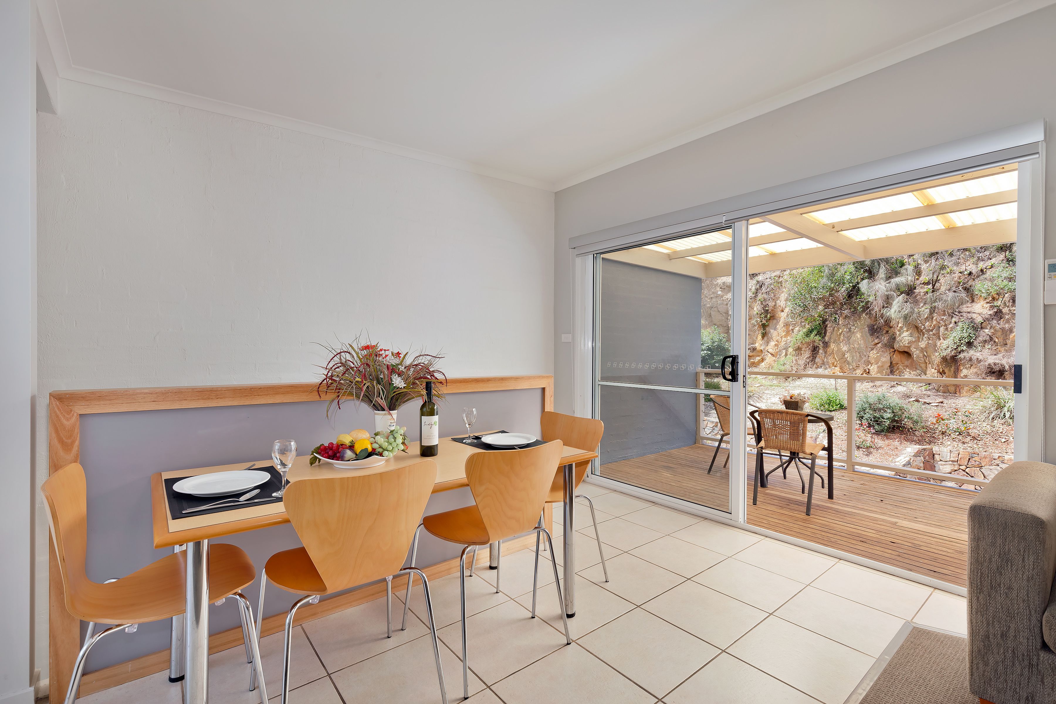 A dining area with a table set for four, a vase with flowers, and a bottle of wine.