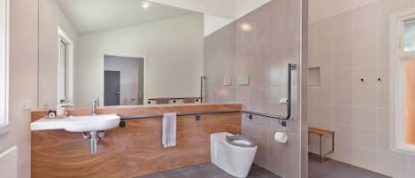 A modern bathroom with a wooden vanity, a white sink, a toilet, and a small bench.