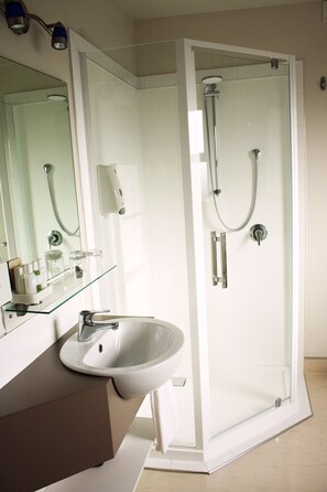 A modern bathroom with a glass-enclosed shower, a white sink, and a glass shelf with toiletries. - Hawera Central Motor Lodge (Hawera)