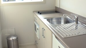 A compact kitchen with a window, a sink, a trash can, and a stove. - Hawera Central Motor Lodge (Hawera)