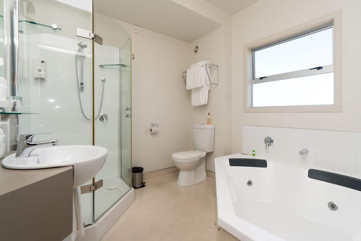 Ein modernes Badezimmer mit einer gläsernen Dusche, einer weißen Toilette, einer gro ßzügigen Badewanne und einem Fenster mit Tageslicht.