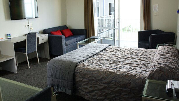 A hotel room with a bed, a desk, a chair, a TV, and a balcony with curtains. - Hawera Central Motor Lodge (Hawera)